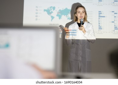 Young Blond-haired Medical Student In Lab Coat Speaking Into Microphone While Giving Speech At Conference