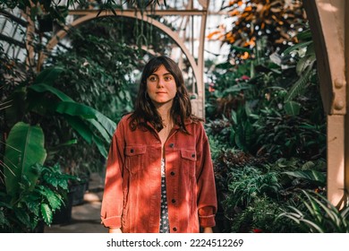 young blue eyed brunette caucasian woman in red corduroy coat standing calmly inside a botanic garden with lots of plants lit by sunlight, botanic garden christchurch, new zealand - Shutterstock ID 2224512269