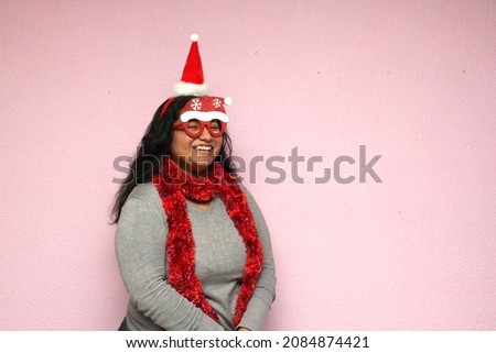 Young body positive fat latina woman with Christmas hat and glasses shows her enthusiasm for the arrival of December and celebrating Christmas
