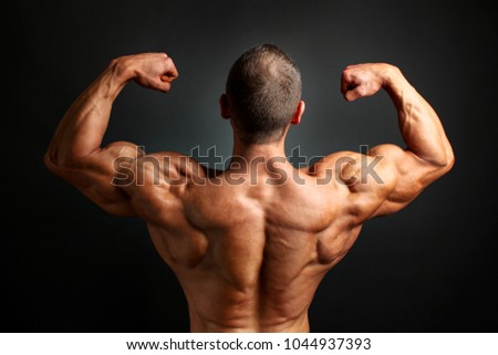 Young bodybuilder man flexing back double bicpes pose, showing his huge trapezius, rhomboid, levator and latissimus dorsi muscles. Studio shot on black background.