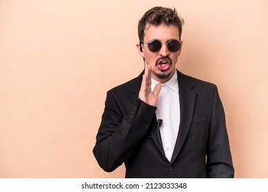 Young Bodyguard Caucasian Man Isolated On Beige Background Is Saying A Secret Hot Braking News And Looking Aside