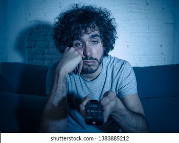 Young bored man on couch using TV remote control zapping for another movie or show late at night. Looking disinterested and sleepless. In entertainment People insomnia and Sedentary lifestyle concept. - Shutterstock ID 1383885212
