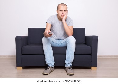 Young Bored Man Sitting On Sofa And Watching Tv