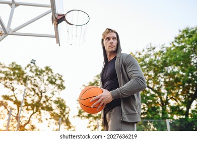 Young Bottom View Sporty Sportsman Man 20s Wear Grey Sports Clothes Hood Training Holding In Hand Ball Shooting Free Throw Play At Basketball Game Playground Court. Outdoor Courtyard Sport Concept.