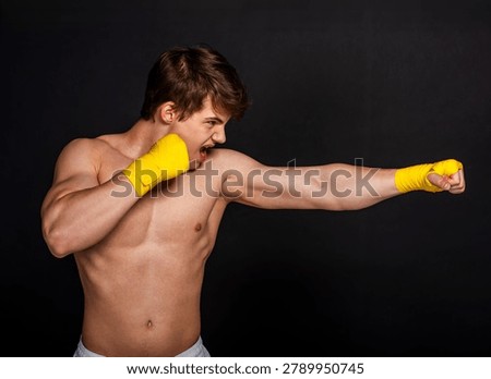 Young boxer practicing a powerful punch with wrapped hands against a dark background.