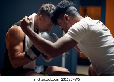 Young boxing player getting encouraged by his coach, sitting in dressing room. Mental preparation, holding heads against each other. - Powered by Shutterstock