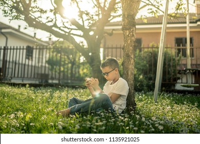 Young boy alone playing with smartphone. Pre teen with glasses sitting outdoor play with phone in hand. The use of the smartphone isolates the boy from the surrounding reality. - Powered by Shutterstock