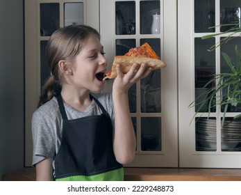 A young boy in an apron holds in his hands and defiantly eats a home-made pizza against the background of a kitchen cabinet. - Powered by Shutterstock