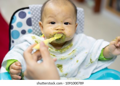 Young boy Asian infant happily eating soft meal messy and dirty around his face