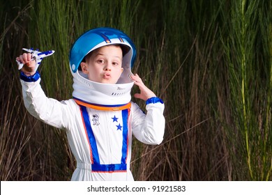 Young Boy In An Astronaut Suit Playing With A Toy Airplane.