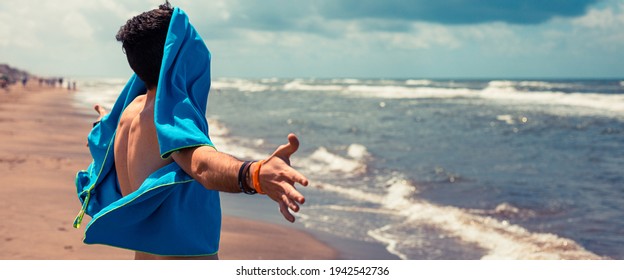 Young boy with a beach towel in his face because there is too much wind in the shore - Powered by Shutterstock