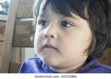 Young Boy Bites His Lip While Watching TV On The Kitchen And Eating Chocolate