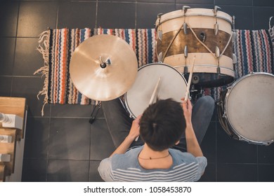 Young boy in blue stripped t-shirt plays on red vintage drums, snare, hi-hat, bass drum in the house with stripped colorful carpet