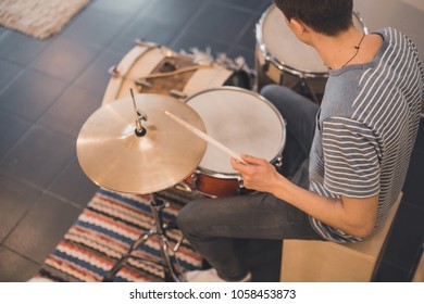 Young boy in blue stripped t-shirt plays on red vintage drums, snare, hi-hat, bass drum in the house with stripped colorful carpet