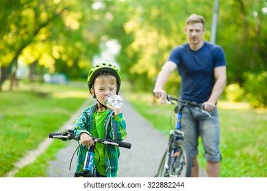 young boy with a bottle of water is learning to ride a bike with his father
