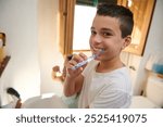 Young boy brushing his teeth, smiling happily in a well-lit bathroom, promoting good dental hygiene habits.