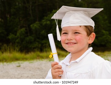 Young boy with cap and gown and certificate for preschool graduation