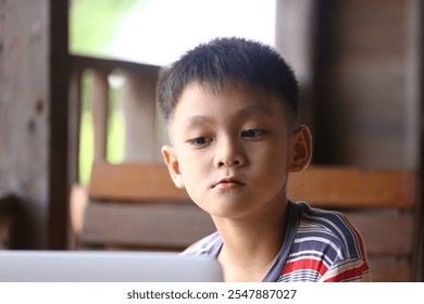 A young boy is captivated while using a laptop at home. His focused expression highlights the connection between childhood and modern technology in a relaxed setting.