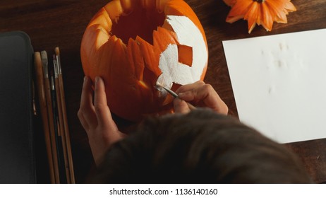 Young boy carving and painting a pumpkin for Halloween on a table - Shutterstock ID 1136140160