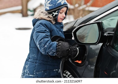 Young Boy Charging Electric Car In The Yard Of House At Winter.