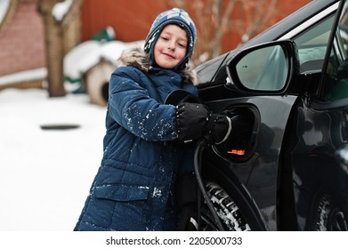 Young Boy Charging Electric Car In The Yard Of House At Winter.