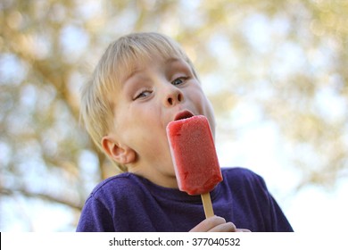 A Young Boy Child Is Making A Funny Face As He Is Eating A Frozen Fruit Popsicle Outside On A Summer Day.