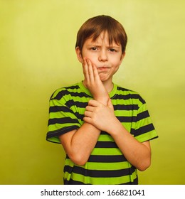 Young Boy Child Toothache Pain In Mouth, Dental Pain, Holding His Cheek On A Green Background