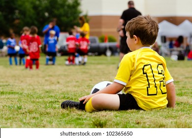 Young Boy Child In Uniform Watching Organized Youth Soccer Or Football Game From Sidelines