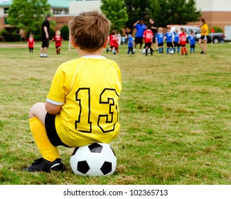 Young Boy Child In Uniform Watching Organized Youth Soccer Or Football Game From Sidelines