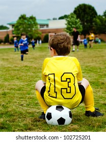 Young Boy Child In Uniform Watching Organized Youth Soccer Or Football Game From Sidelines