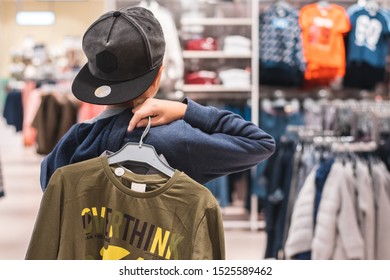 Young boy choosing clothes in the shop by himself, putting on new looks, checking for style. Shopping, black friday, discount and sales concept. - Powered by Shutterstock