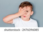 Young boy closed one of his eye with surprised expression on a gray background, shocked amazed terrified gesture