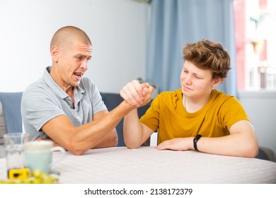 Young boy competing with his father in arm wrestling on kitchen table.