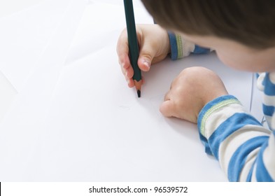 Young boy concentrates while drawing with a green pencil