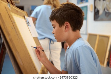 Young boy concentrating on his drawing during an art class, guided by a teacher in a workshop setting. Creative and educational activity for children. - Powered by Shutterstock