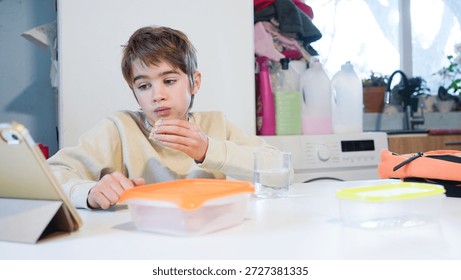 Young boy consuming a snack while absorbed by digital content on a tablet device