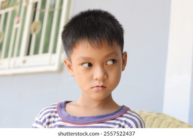 A young boy with a curious expression, wearing a striped shirt, captured in a warm, indoor setting. His thoughtful gaze reflects innocence and playful energy. - Powered by Shutterstock