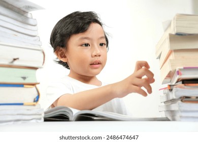 A young boy, with a curious and playful expression, reaches out to a stack of books while studying. Ideal for educational materials, school promotions, and child learning resources. - Powered by Shutterstock