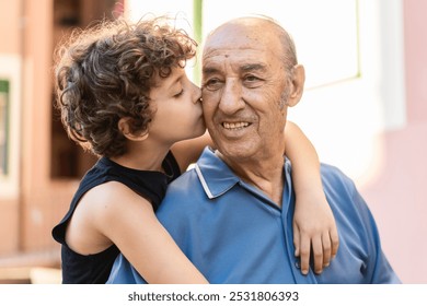 Young boy with curly hair kissing and hugging his smiling grandfather. Close-up of intergenerational affection and family bond outdoors. - Powered by Shutterstock