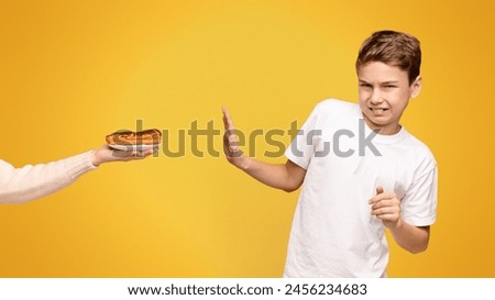 A young boy with a disgusted expression declining a hotdog from an outstretched hand.