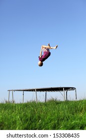 Young Boy Doing A Backflip On A Trampoline On Green Meadow