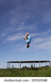 Young Boy Doing A Backflip On A Trampoline On Green Meadow