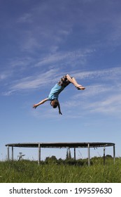 Young Boy Doing A Backflip On A Trampoline On Green Meadow