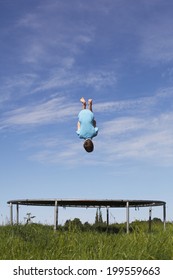 Young Boy Doing A Backflip On A Trampoline On Green Meadow