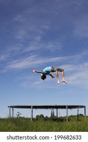 Young Boy Doing A Backflip On A Trampoline On Green Meadow