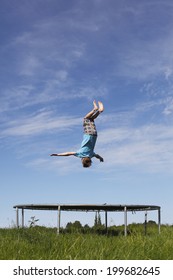 Young Boy Doing A Backflip On A Trampoline On Green Meadow