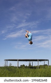 Young Boy Doing A Backflip On A Trampoline On Green Meadow