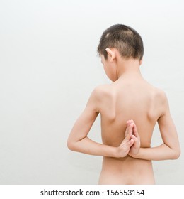 young boy doing yoga exercise in Virasana or Hero Pose with reversed prayer or namaste in studio against a mottled background from behind.