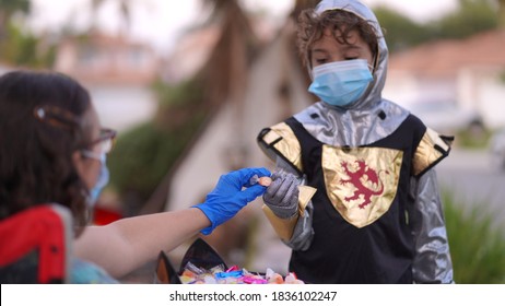 A Young Boy Dressed In Halloween Costume Is Wearing A Face Mask For Trick Or Treating, Takes A Candy From A Person Wearing Mask And Gloves.                               