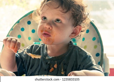 A Young Boy Eating Baked Beans In A Highchair